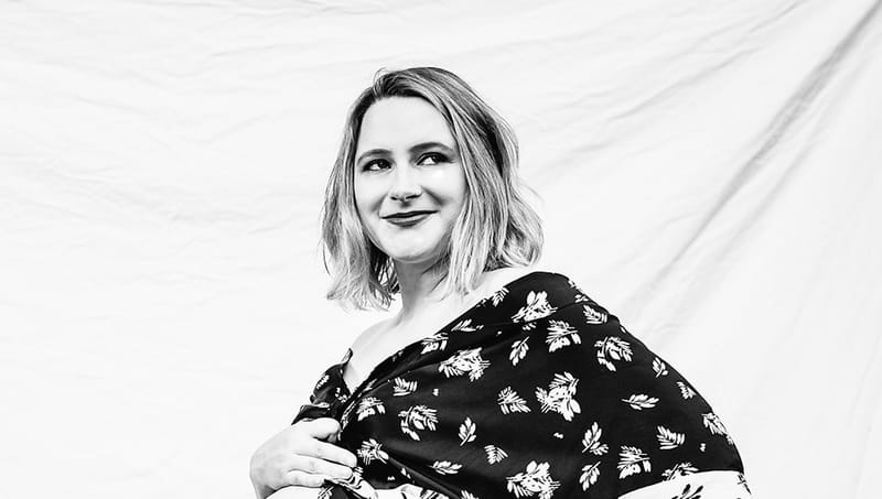 Black and white portrait of Nicole Jones in a floral dress, smiling and looking off camera